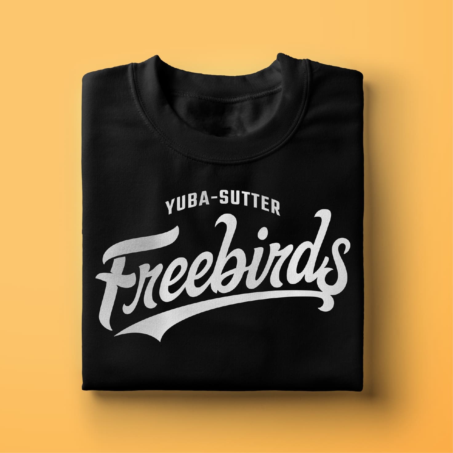 A folded black sweatshirt with YUBA-SUTTER Freebirds printed in bold white script on the front, displayed on a light yellow background.