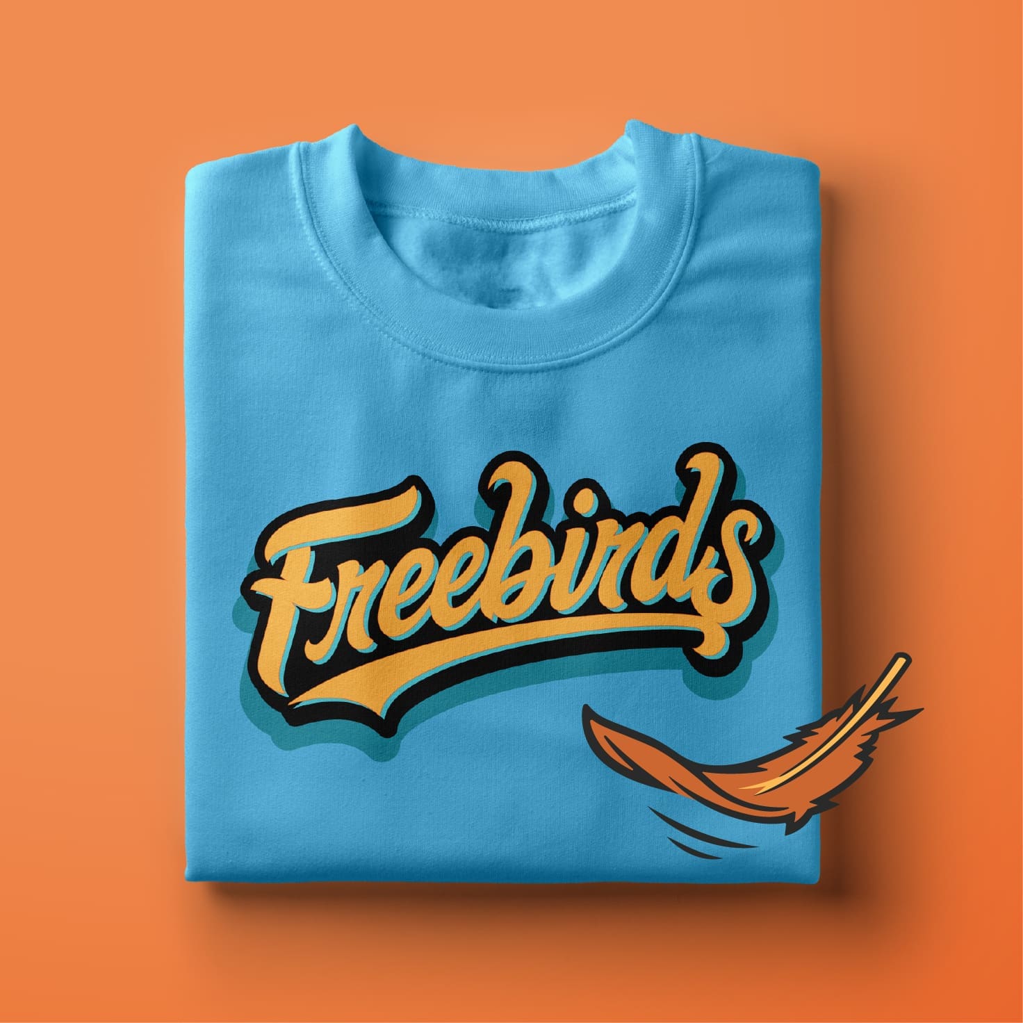 A folded blue t-shirt with the word “Freebirds” in bold, retro-style yellow and black script, accompanied by an orange feather graphic on the lower right. The background is solid orange.
